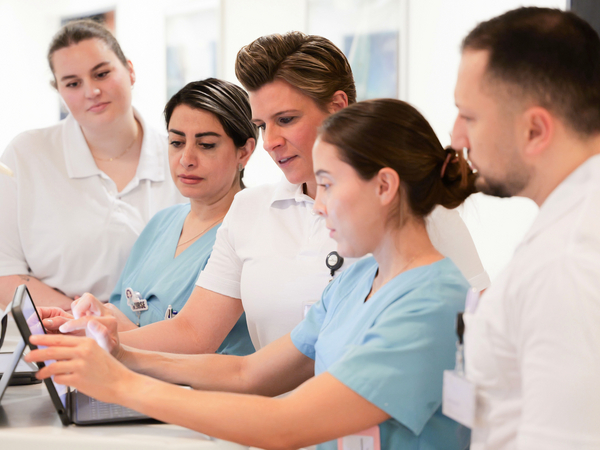Mehrere Fachkräfte aus dem Team um Zentrumsleiterin Dr. med. Julia M. Reinke blicken auf einen Tablet-Computer auf einem Stationswagen in einem Stationsflur und unterhalten sich im auf Hüftprothesen, Knieprothesen und Schulterprothesen spezialisierten Albertinen Endoprothetikzentrum Hamburg Mehrere Fachkräfte aus dem Team um Zentrumsleiterin Dr. med. Julia M. Reinke blicken auf einen Tablet-Computer auf einem Stationswagen in einem Stationsflur und unterhalten sich im auf Hüftprothesen, Knieprothesen und Schulterprothesen spezialisierten Albertinen Endoprothetikzentrum Hamburg